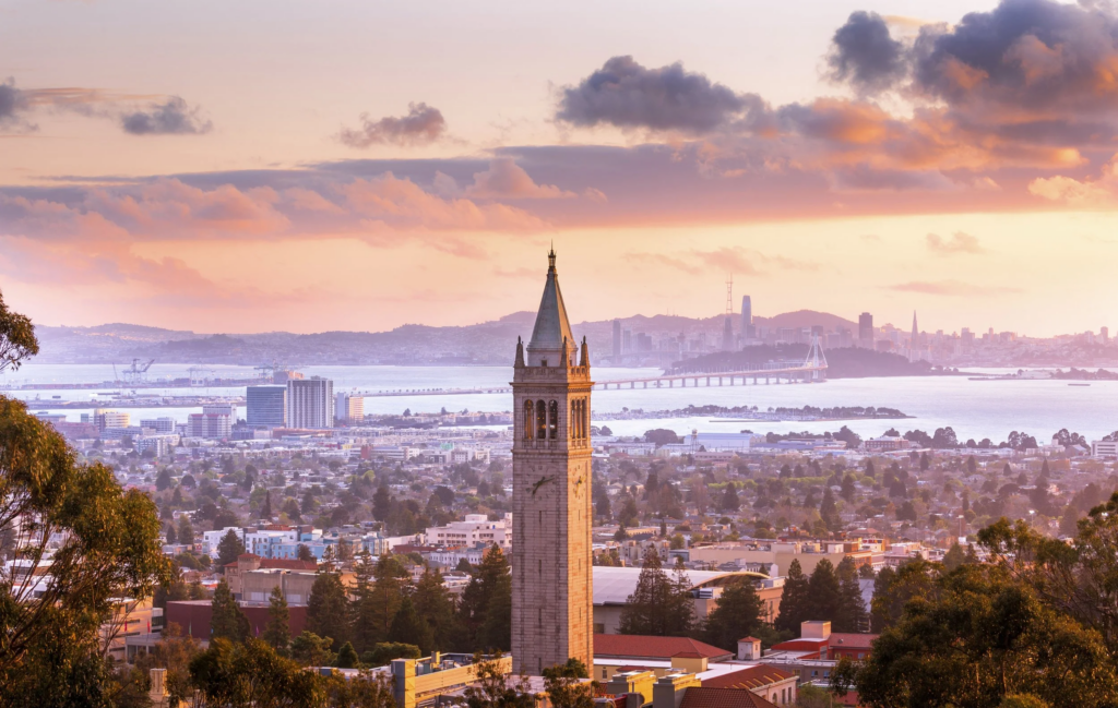 UC Berkeley Sather Tower campanile at sunset with San Francisco Bay Bridge and skyline in background — personal injury attorney John J. Roach serves accident victims throughout Berkeley and the East Bay