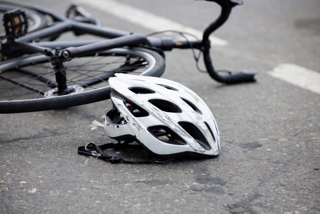 Casco de ciclista dañado y bicicleta junto a la acera después de un accidente — evidencia física crítica que documenta la fuerza del impacto en casos de lesiones de ciclistas hispanos