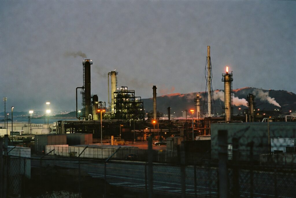 Refinería Chevron en Richmond CA al atardecer — donde trabajadores hispanos enfrentan riesgo significativo de accidentes industriales, exposición química, y lesiones por equipo pesado en una de las instalaciones petroquímicas más grandes del East Bay