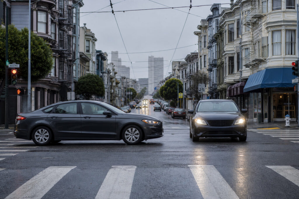 Cars at a wet San Francisco intersection on a hill street with overhead wires