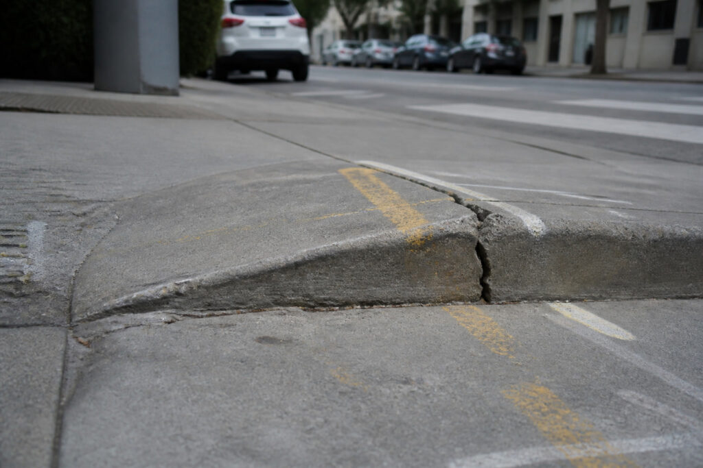 Height difference on a cracked San Francisco sidewalk with Public Works paint marks