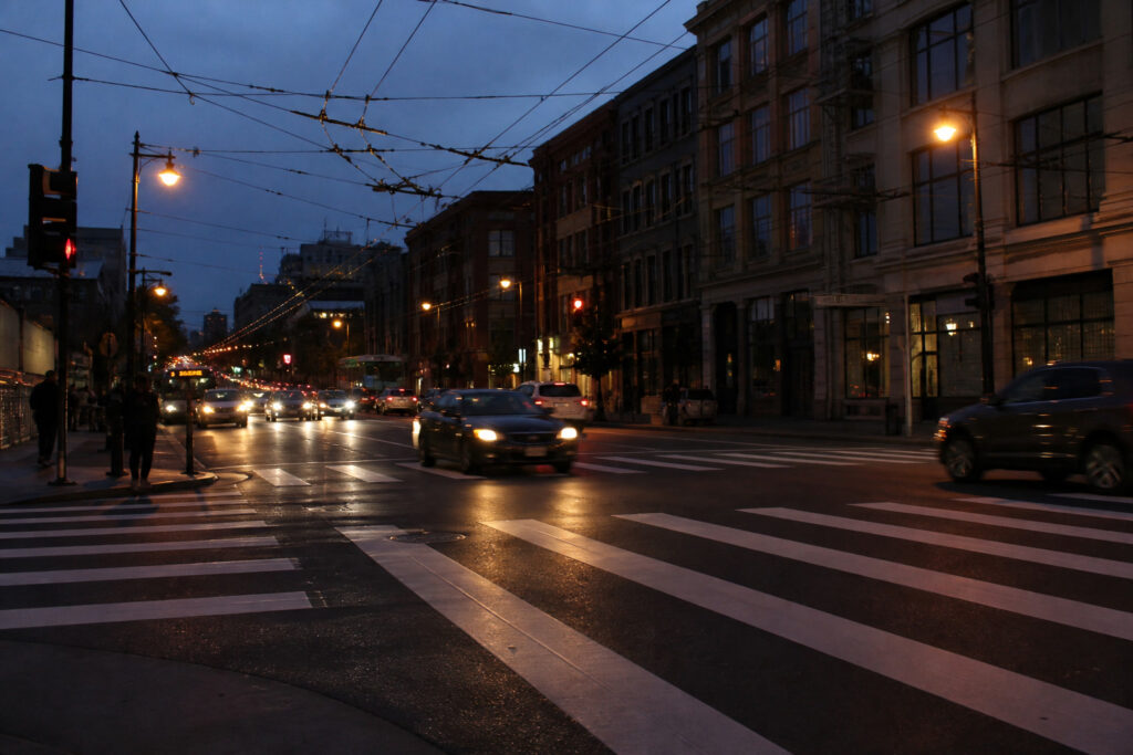 Painted San Francisco crosswalk at dusk as headlights hit the evening commute