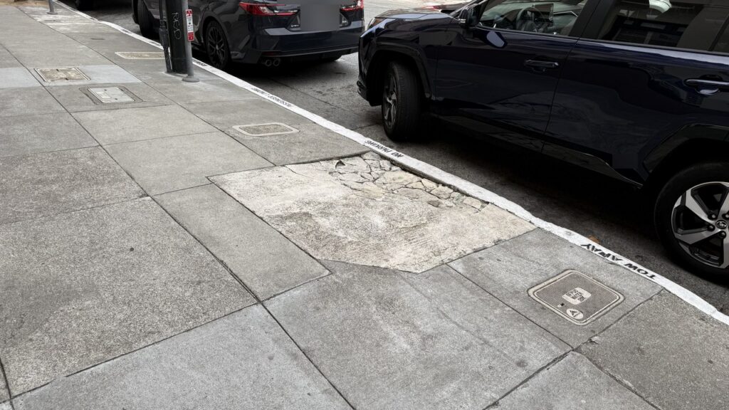 A pedestrian's view of a broken sidewalk slab beside a white curb stenciled NO PARKING on Sutter Street, San Francisco